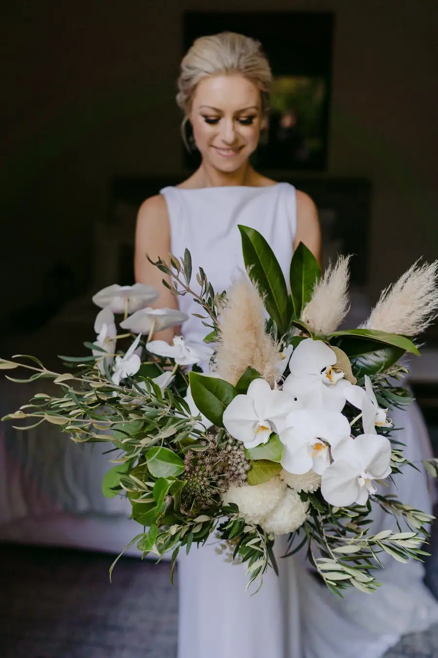 Bride looking down at a large bouquet of white flowers and greenery