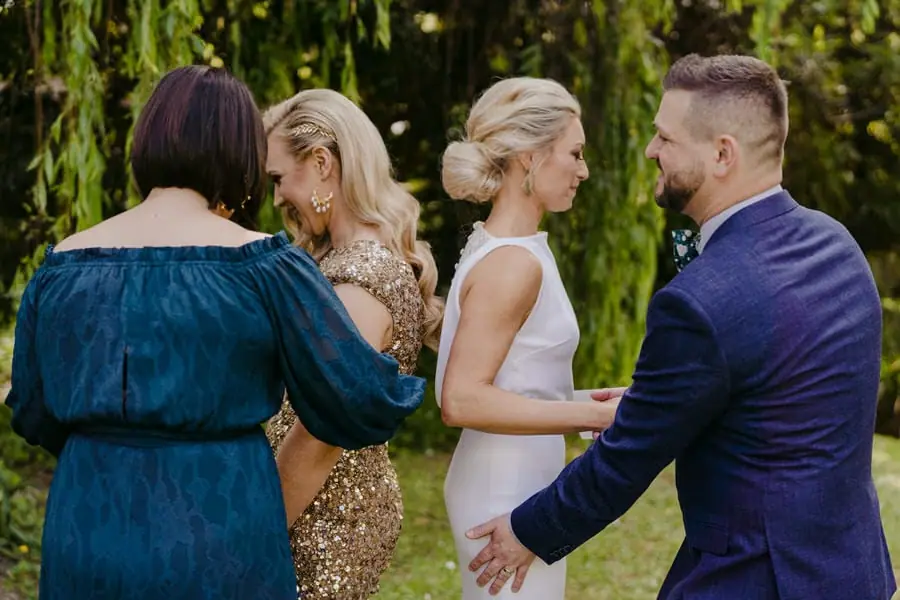 Friends guiding two brides toward one another in a leafy garden