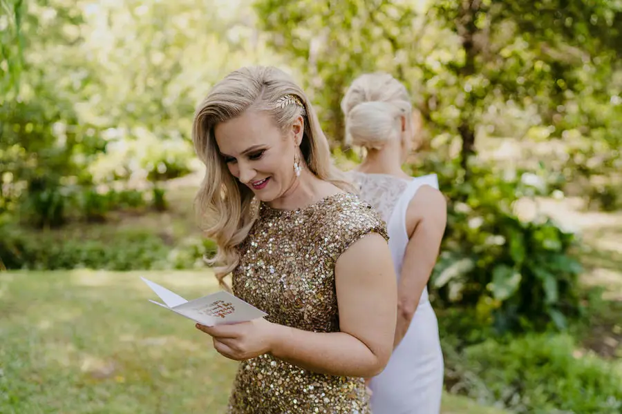 Bride in a gold dress smiling while reading a card with her partner behind her