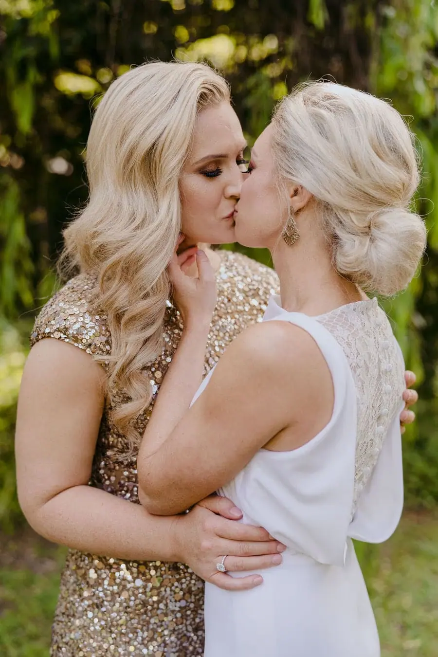 Two brides kissing beneath green willow branches
