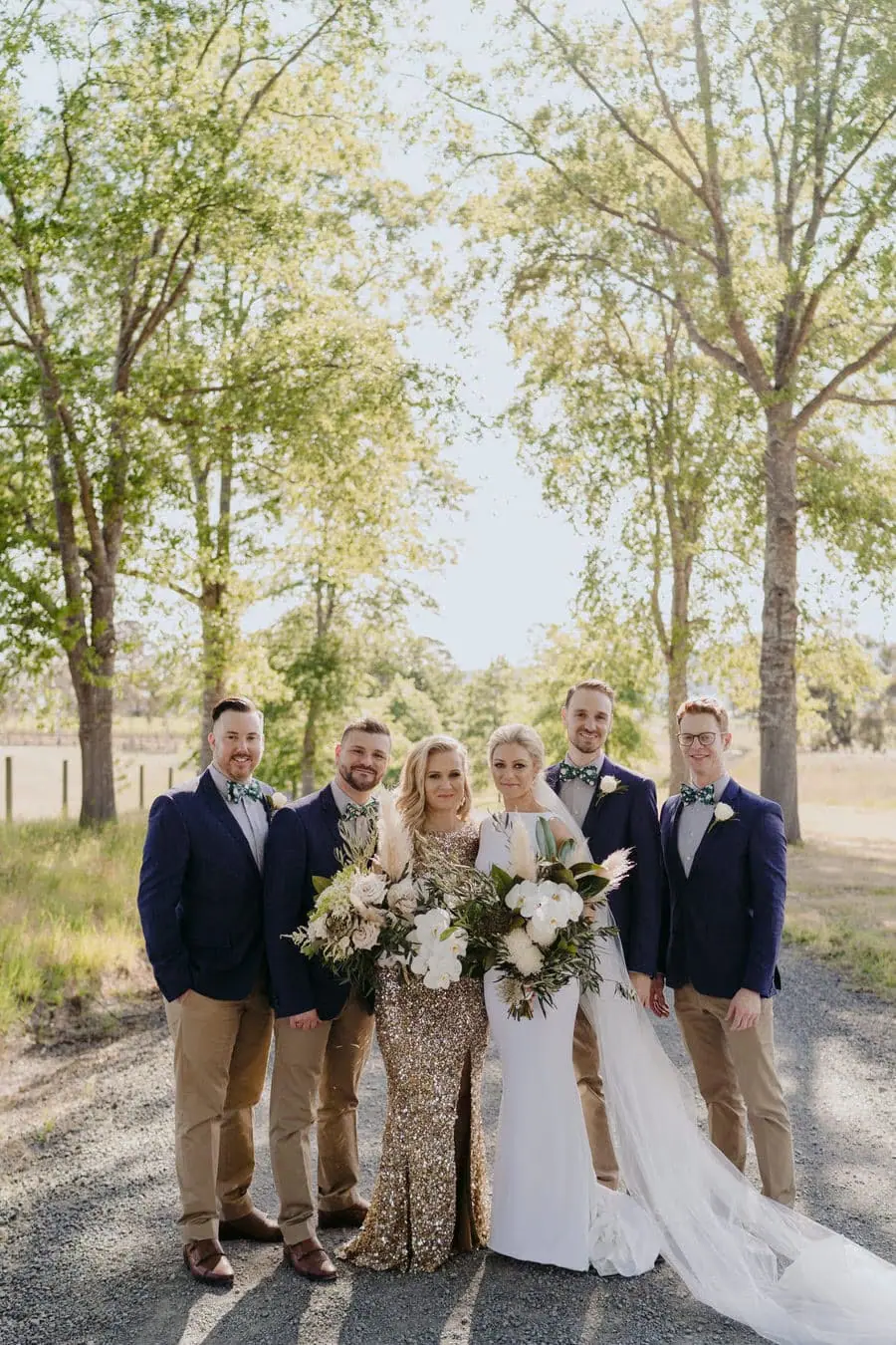 Bride posing with four men in blue jackets on a tree-lined driveway