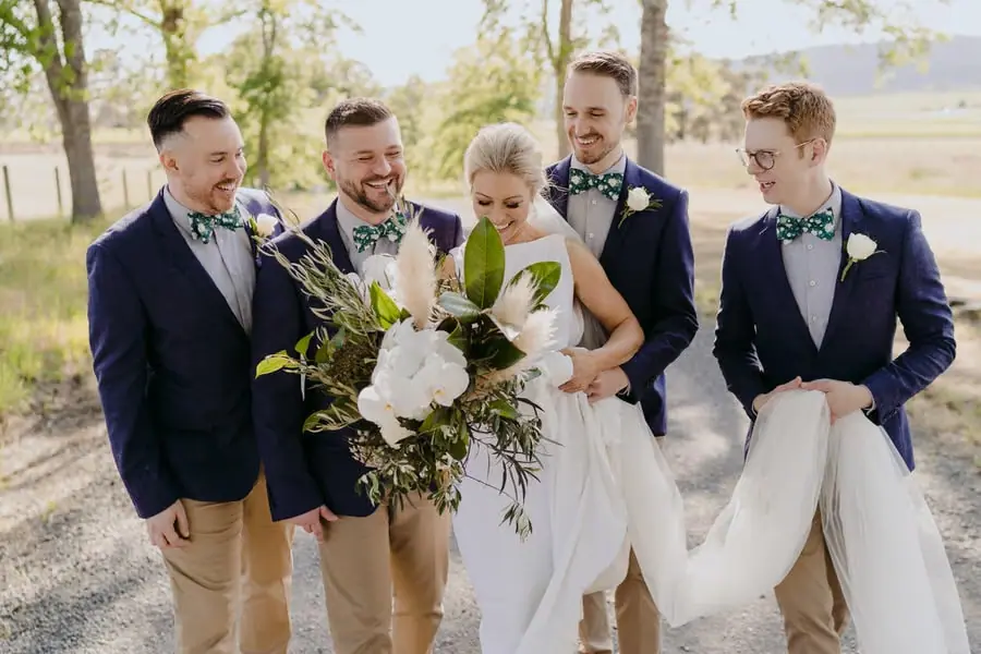 Bride laughing with four men while holding a large white bouquet