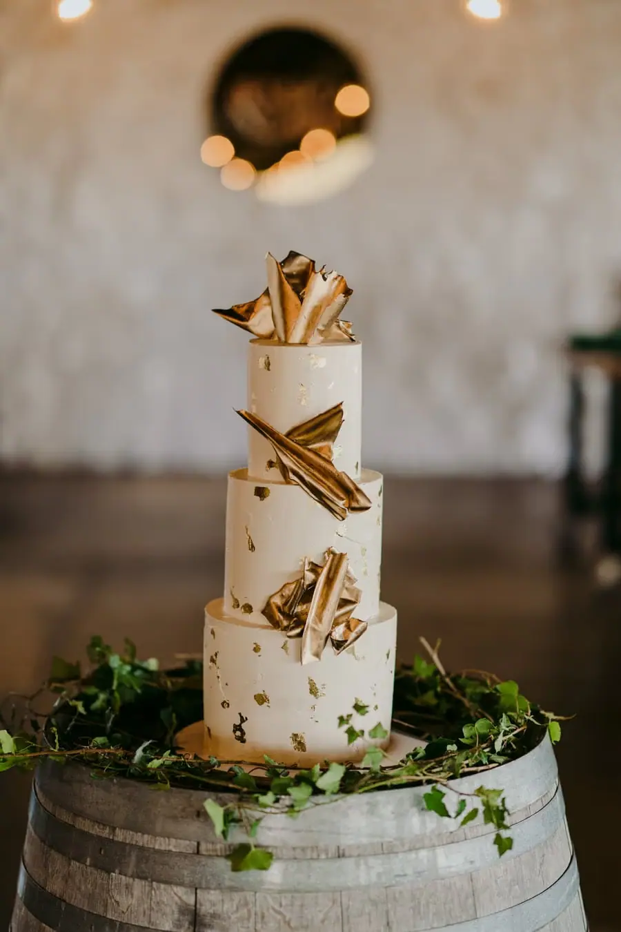 Three-tier white wedding cake decorated with gold accents on a wine barrel