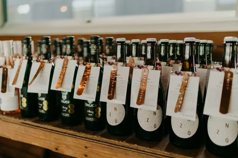 Rows of wine bottles with individual paper tags arranged on a wooden table