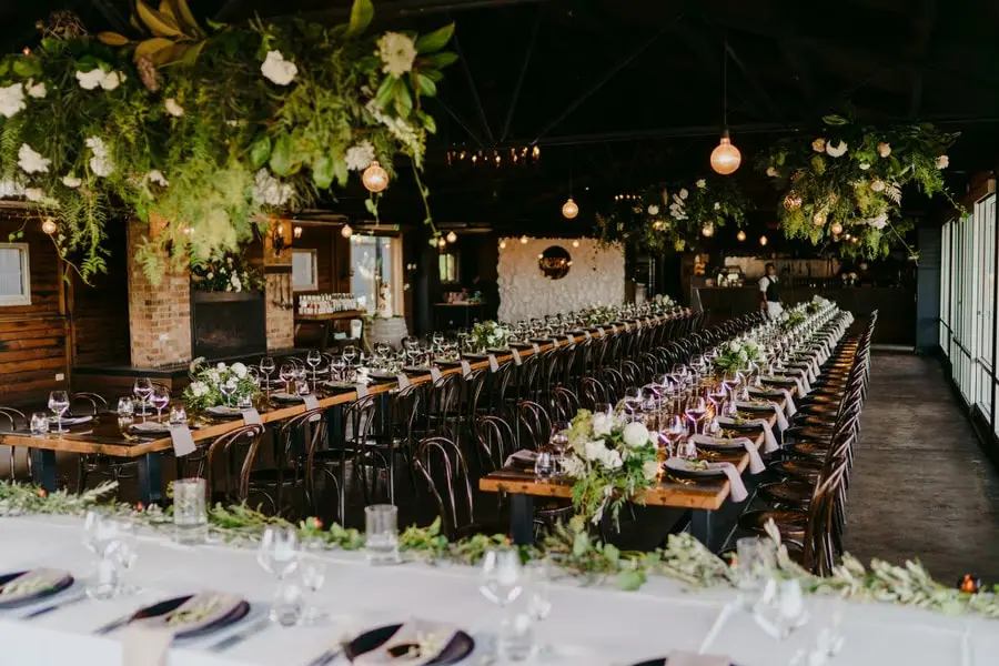 Wide view of long reception tables beneath hanging flowers and exposed beams