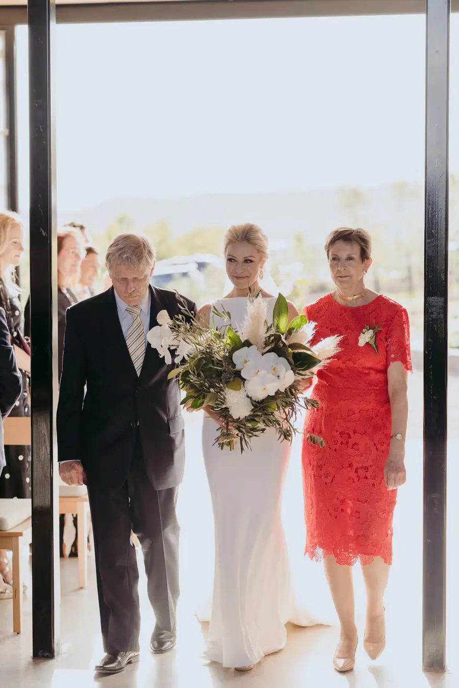 Bride in a white dress walking through a doorway between two companions