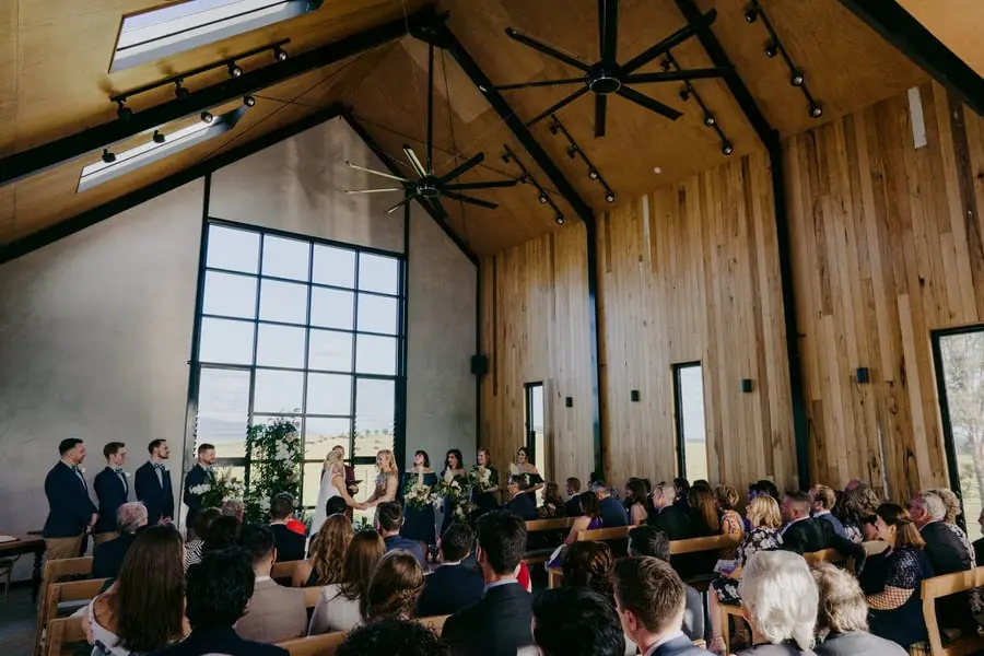 Guests seated inside a timber-lined ceremony hall beneath a high roof
