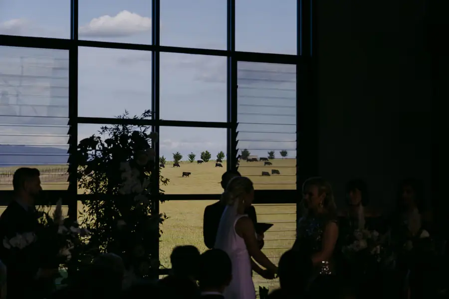 Two brides silhouetted beside a tall window overlooking farmland
