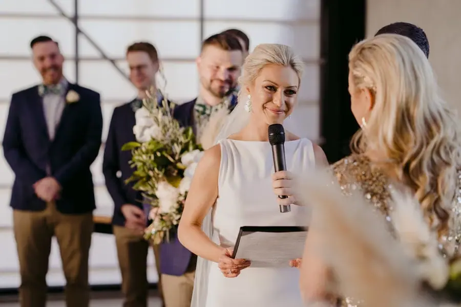 Bride in a white dress reading vows into a microphone toward her partner