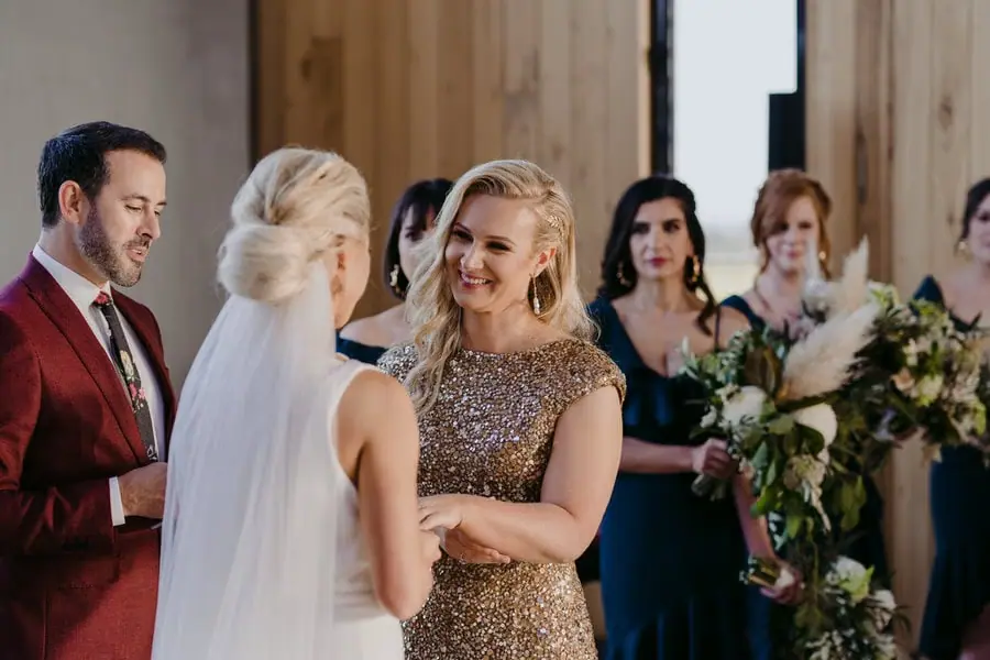 Bride in a gold dress smiling at her partner during the ceremony