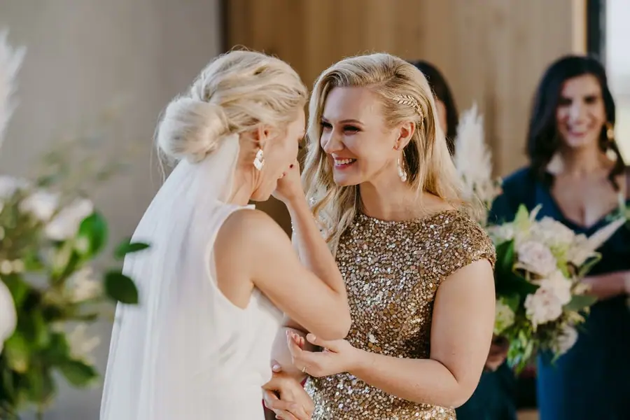 Two brides smiling closely together while holding one another's arms