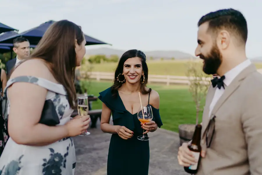 Three wedding guests chatting with drinks beside the reception terrace
