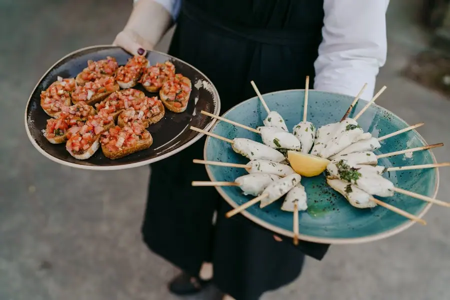 Server carrying platters of tomato-topped bread and white skewered appetisers