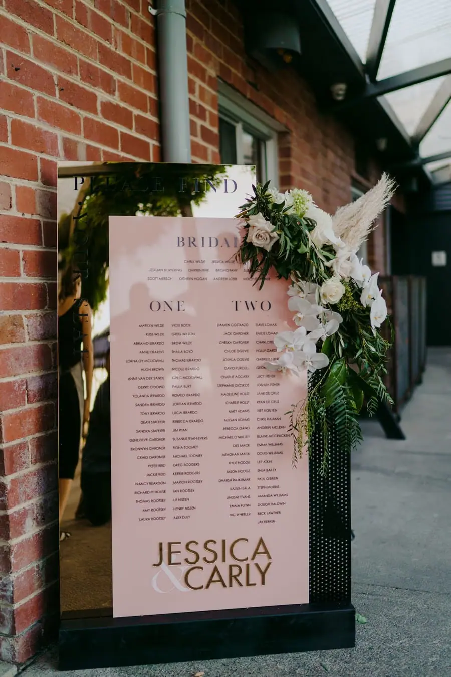 Flower-decorated wedding seating chart beside a brick wall