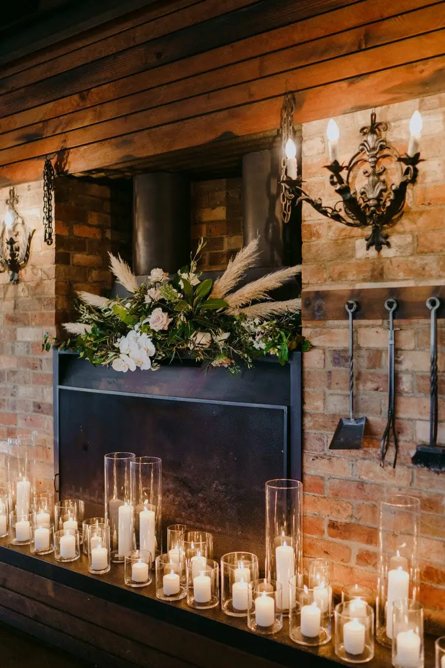 Glass candle holders glowing beneath flowers on a brick fireplace