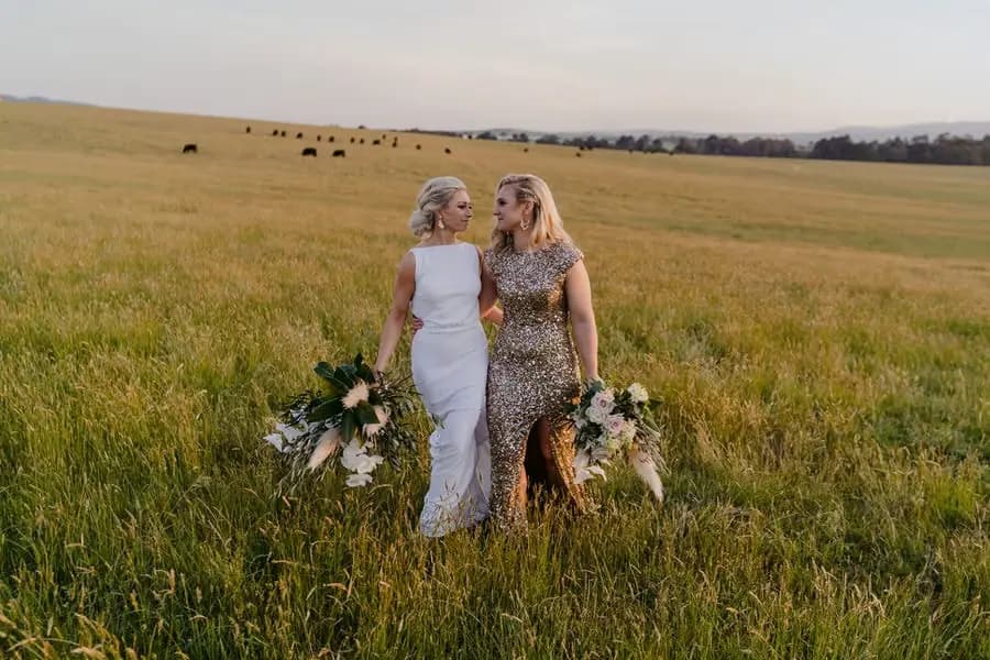 Two brides standing together with bouquets in a rolling grassy field