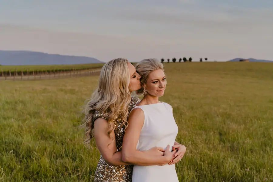 Bride in a gold dress embracing her partner from behind in a field