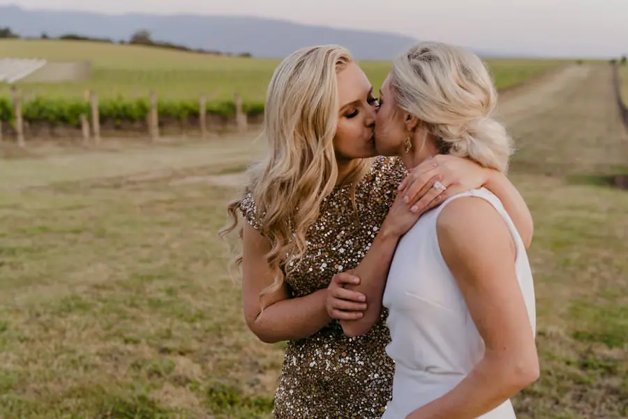 Two brides kissing with a vineyard and distant hills behind them