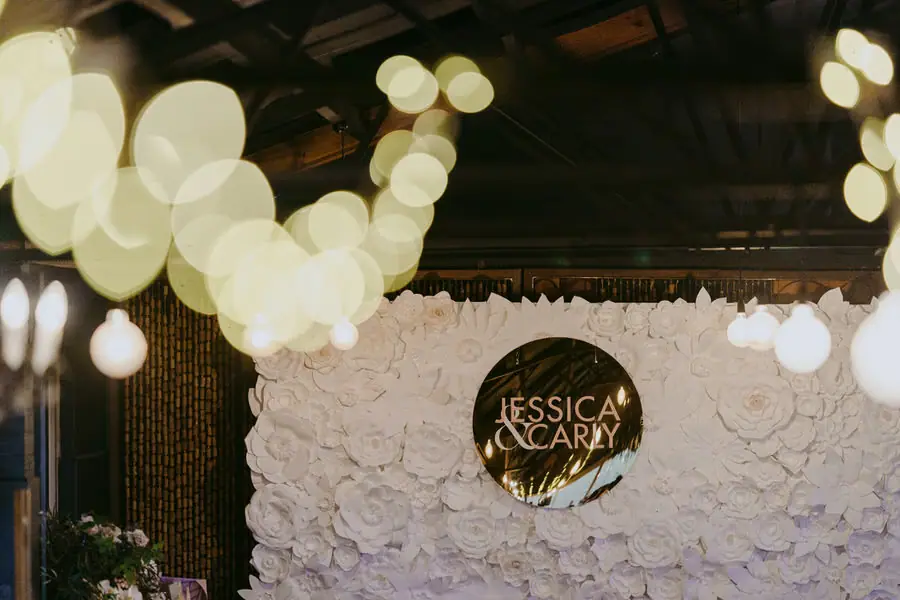 Round personalised wedding sign on a white flower-covered backdrop beneath glowing lights
