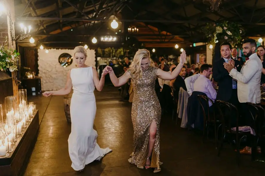 Two brides entering the reception hand in hand while guests applaud