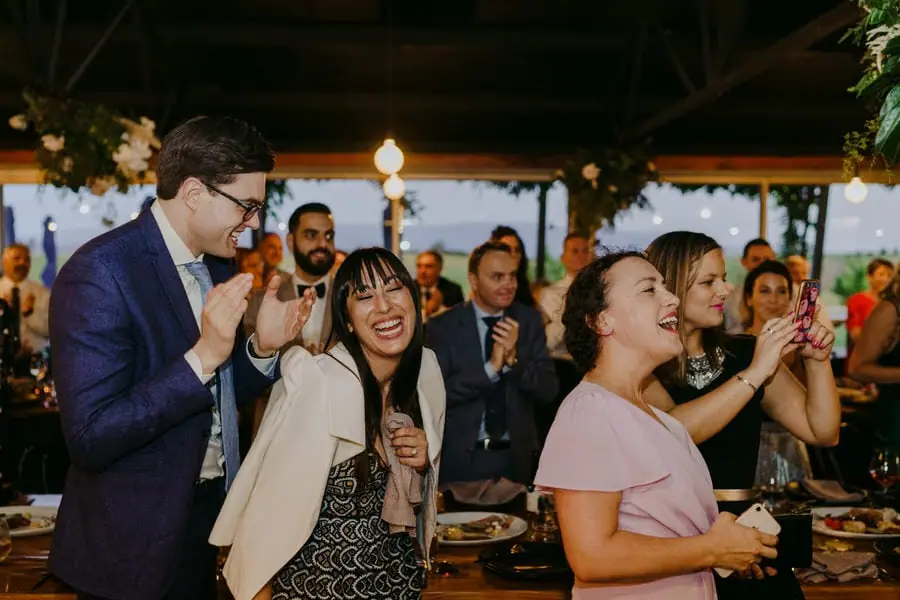 Wedding guests laughing and applauding beneath warm reception lights
