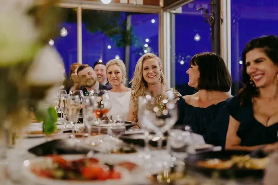 Two brides smiling among friends seated at a long reception table