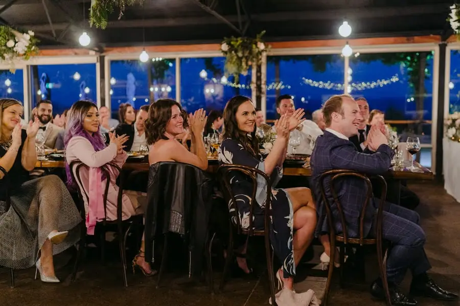 Wedding guests applauding from their seats beside large windows