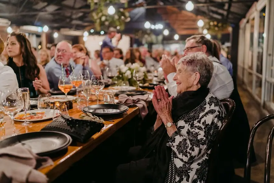 Older guest applauding beside a long flower-decorated reception table