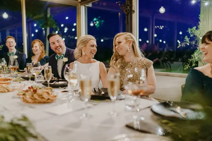 Two brides smiling together while seated among wedding guests