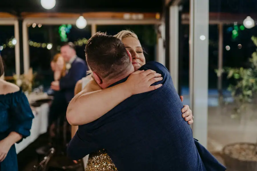 Bride in a gold dress hugging a guest in a blue jacket
