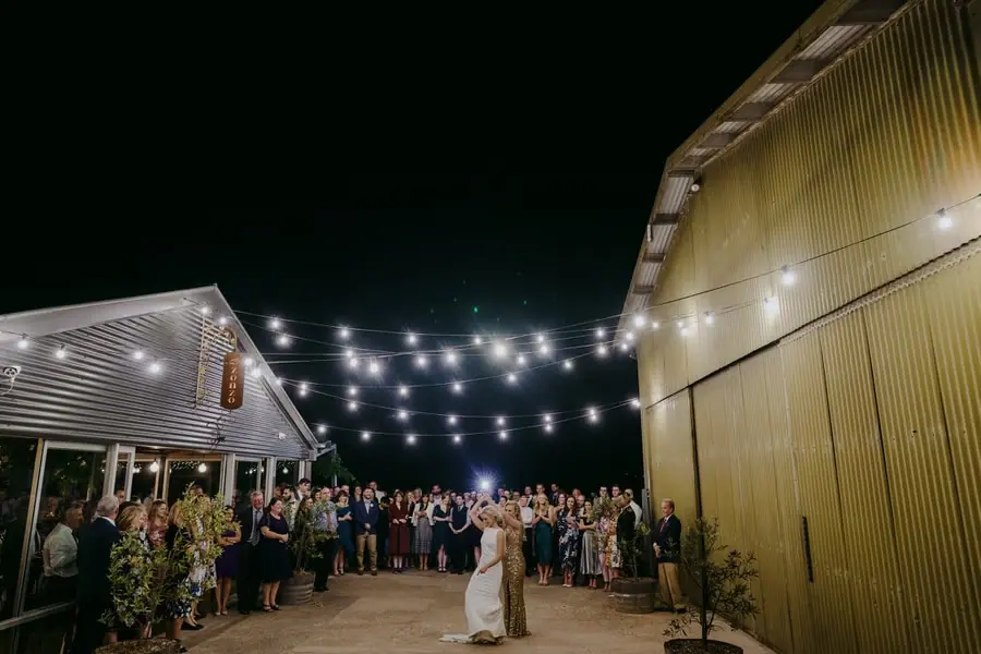 Wide view of the couple dancing between buildings beneath glowing strings of lights