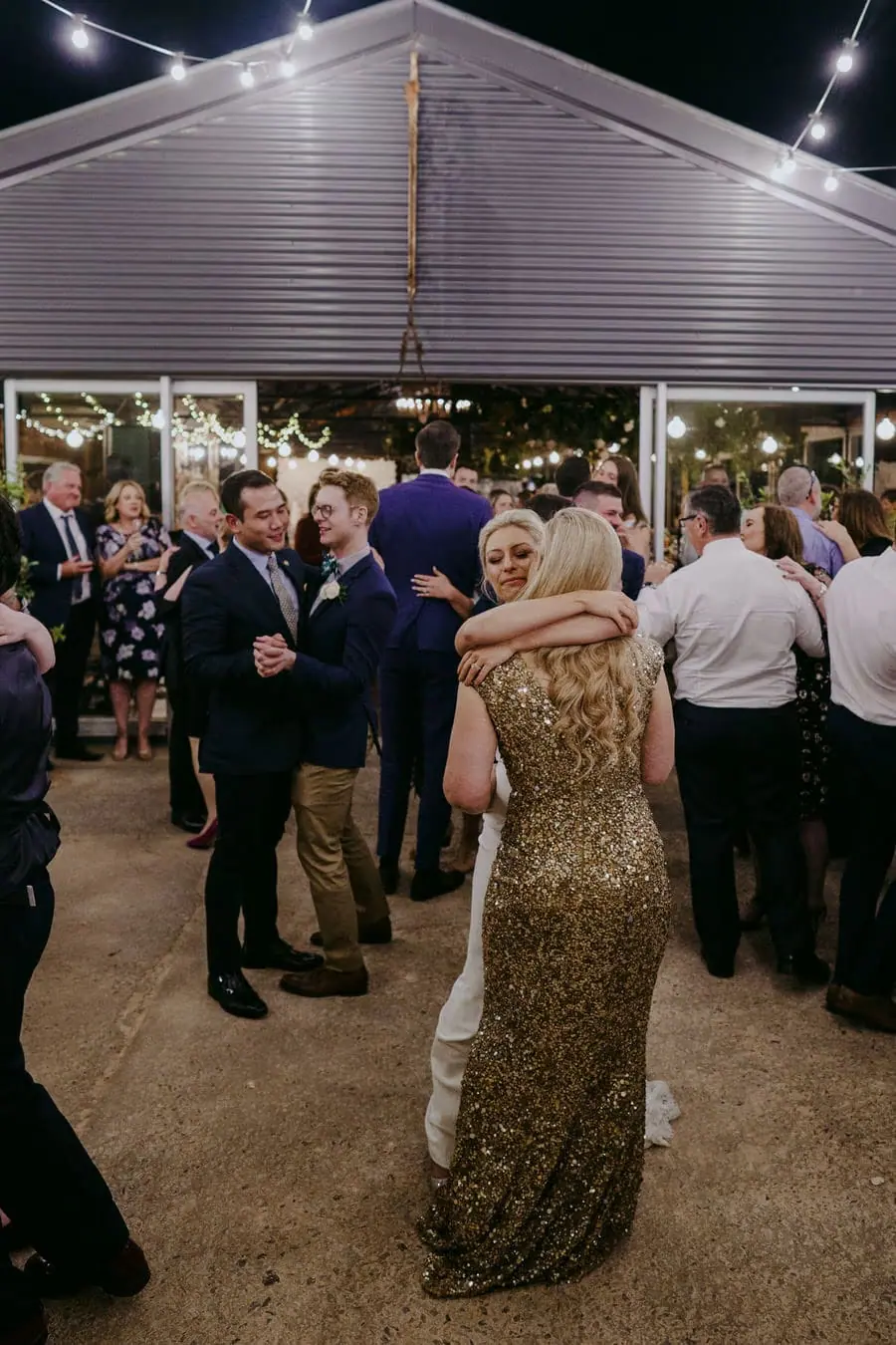 Bride in a gold dress embracing her partner among dancing guests outdoors
