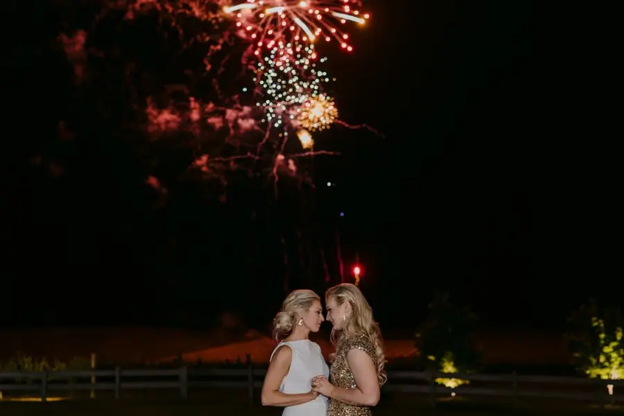 Two brides kissing beneath bright red fireworks