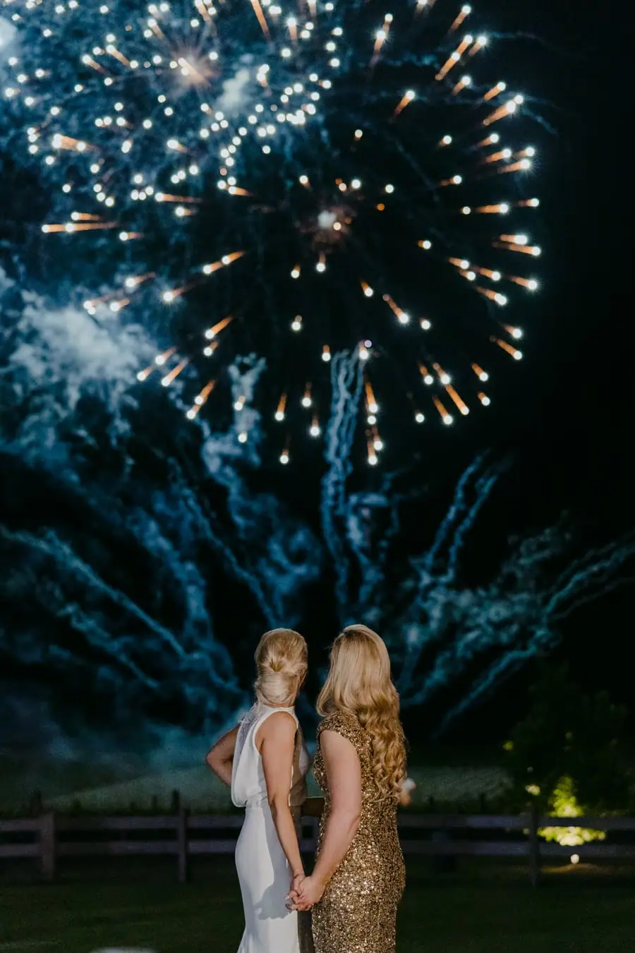 Two brides embracing beneath sparkling fireworks at night