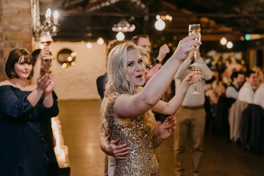 Two brides raising champagne glasses as guests applaud