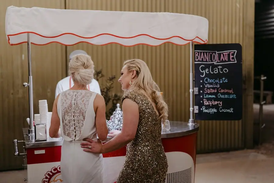 Two brides standing beside an outdoor gelato cart