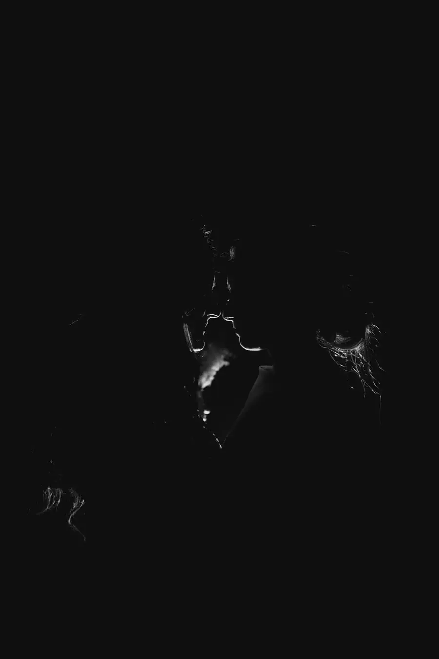 Black-and-white close silhouettes of two brides touching foreheads against faint backlight