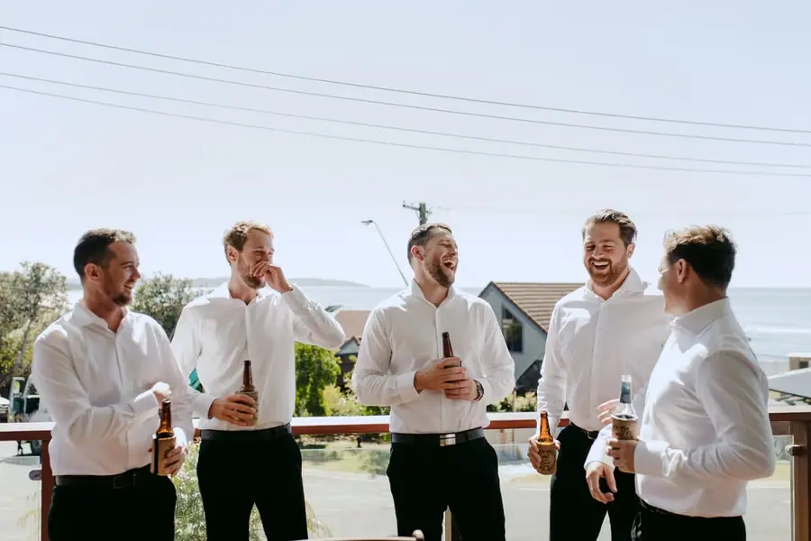 Men in white shirts laughing together on a sunny balcony