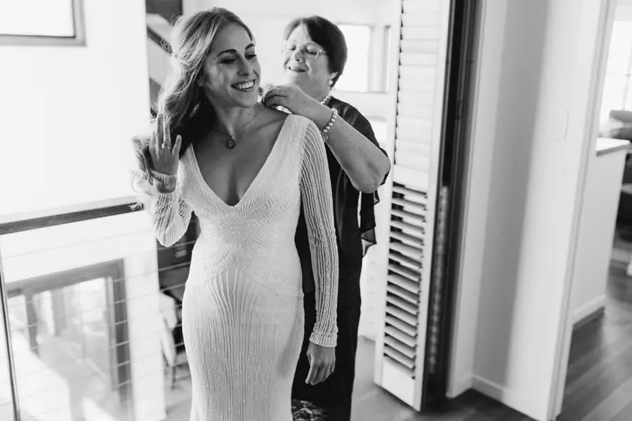 Black-and-white photograph of a woman helping the bride fasten her dress