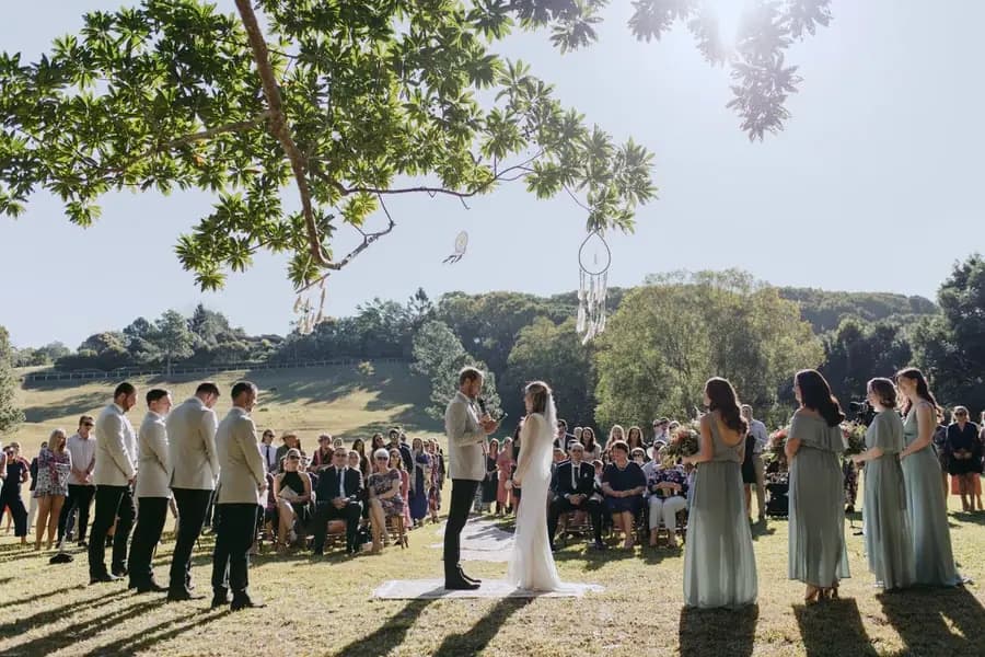 Bride and groom facing each other beneath a tree as guests watch