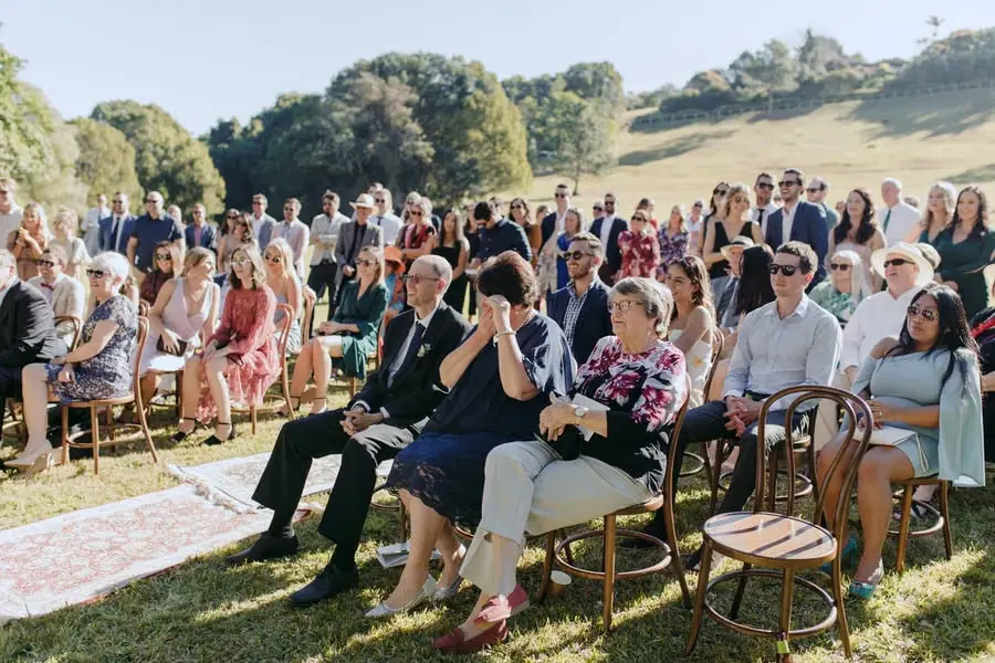Rows of seated guests watching the ceremony beside a grassy hillside
