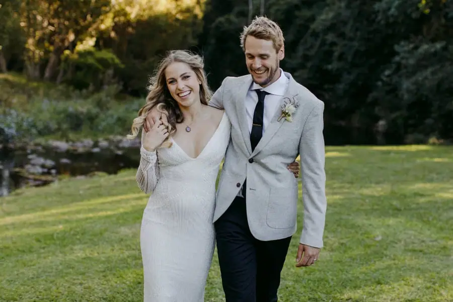 Bride and groom smiling while walking across a lawn