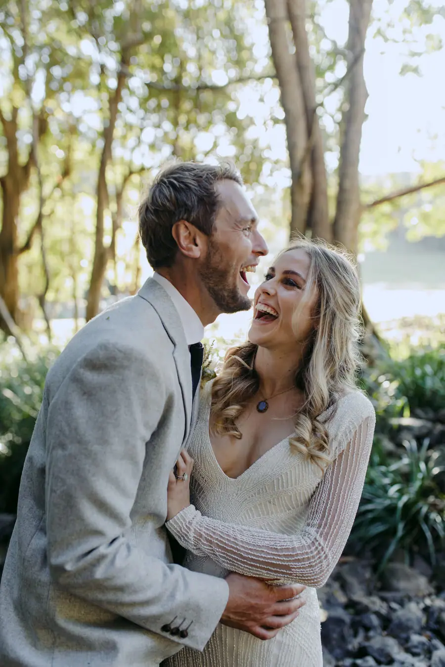 Bride laughing as the groom kisses her beside the creek