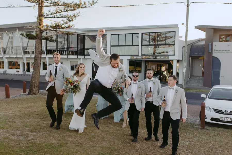Wedding party celebrating outside a building as one groomsman jumps