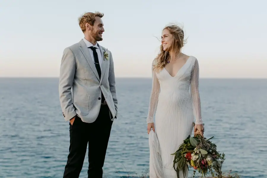 Bride and groom facing each other with the sea behind them
