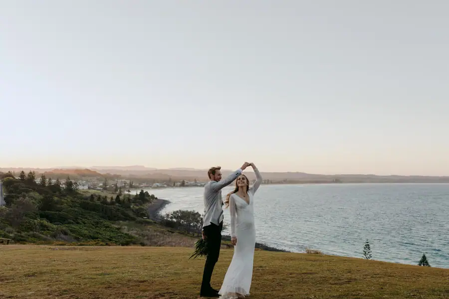 Groom twirling the bride on a grassy headland at sunset