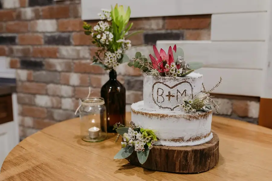 Small wedding cake decorated with flowers and initials on a wooden stand