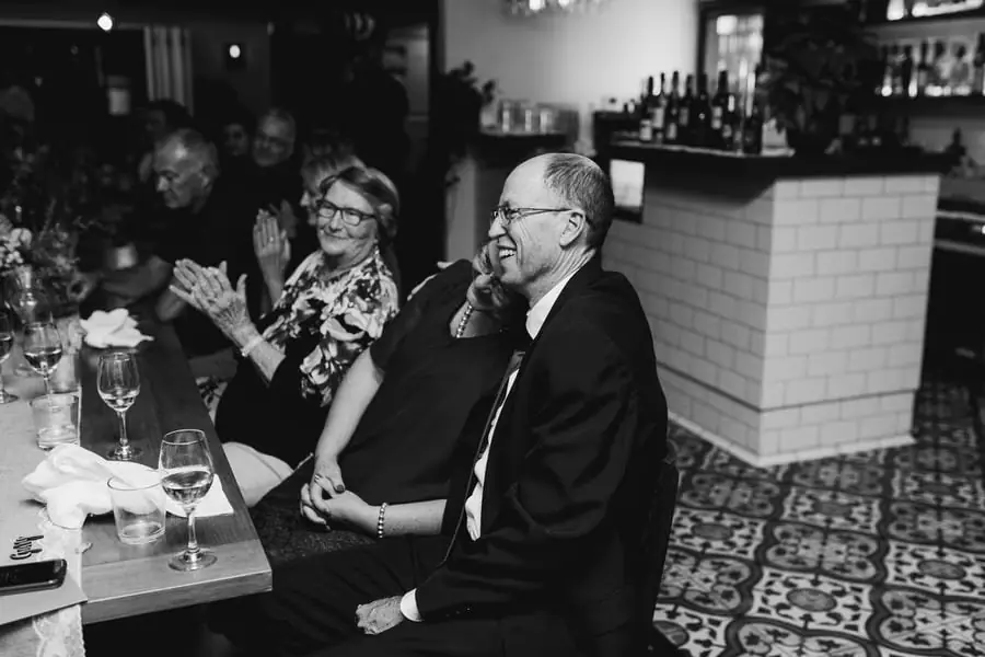 Black-and-white photograph of guests laughing and applauding at a table