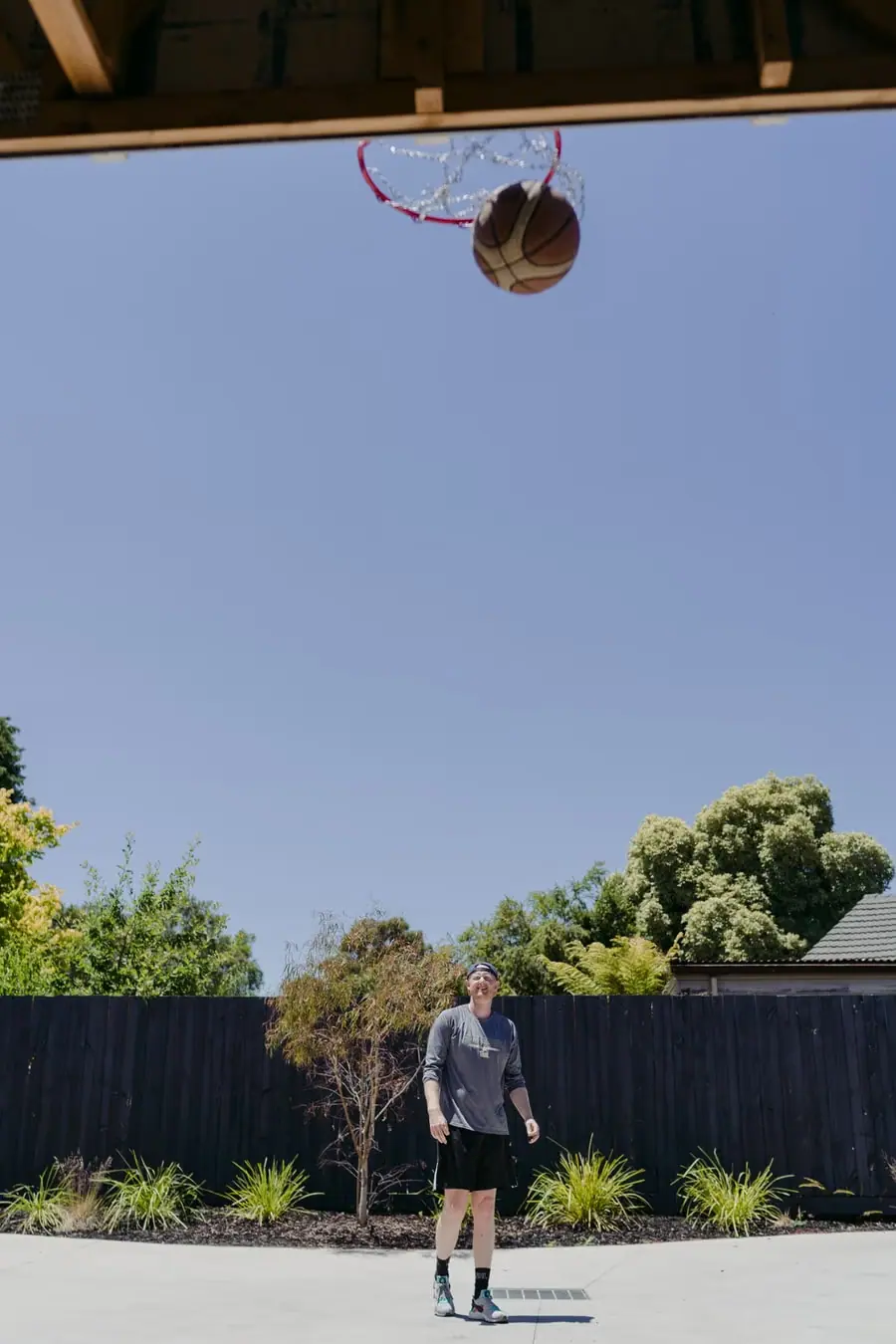 Basketball dropping through a hoop above a man in a sunny courtyard
