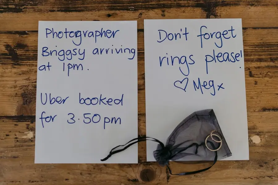 Handwritten wedding reminders and two rings resting on a wooden table